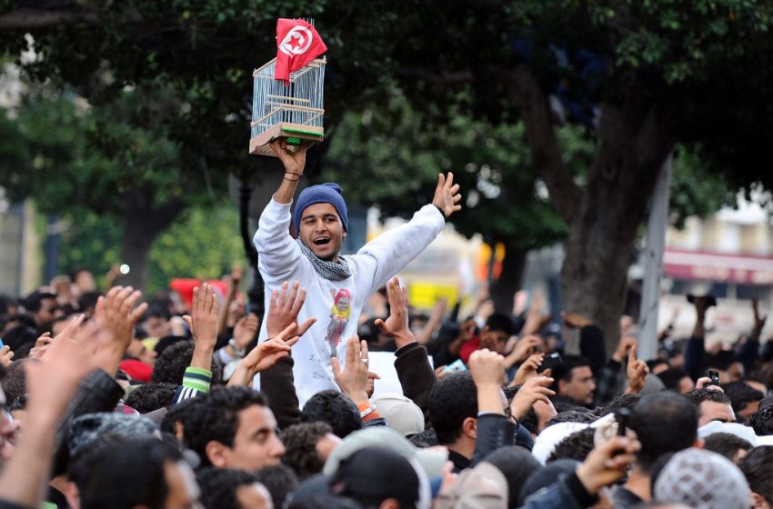 Le manifestant tunisien Wadii Jelassi brandit une cage et le drapeau national lors d’un rassemblement le 14 janvier 2011 devant le ministère de l’Intérieur à Tunis, réclamant la démission de Zine El Abidine Ben Ali.