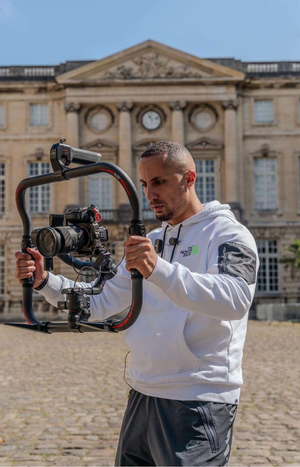 Amine Kassid tenant une caméra montée sur stabilisateur devant un château français.