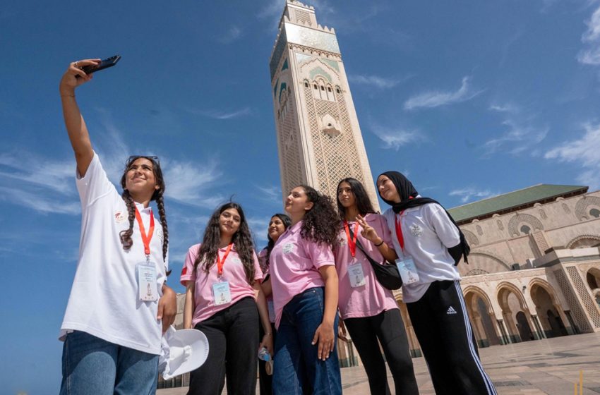 Adolescentes prenant un selfie devant la Grande Mosquée Hassan II de Casablanca, camp d’été Bayt Mal Al‑Qods, août 2026.